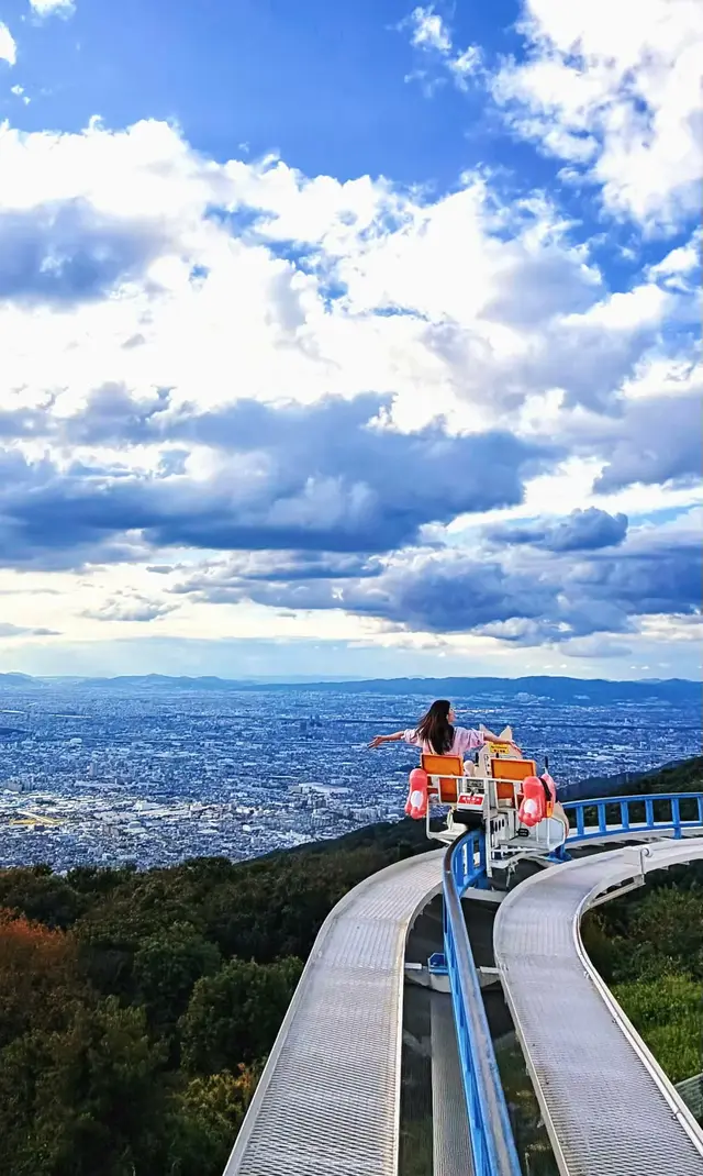 脚踏车沿弯曲高架轨道悬在山腰，下方是大阪平原