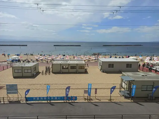 夏天的须磨海岸全景：海滩小屋、遮阳伞、「須磨海岸を笑顔に」横幅